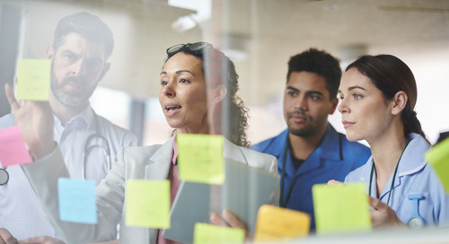 Healthcare professionals looking at sticky notes on a glass wall